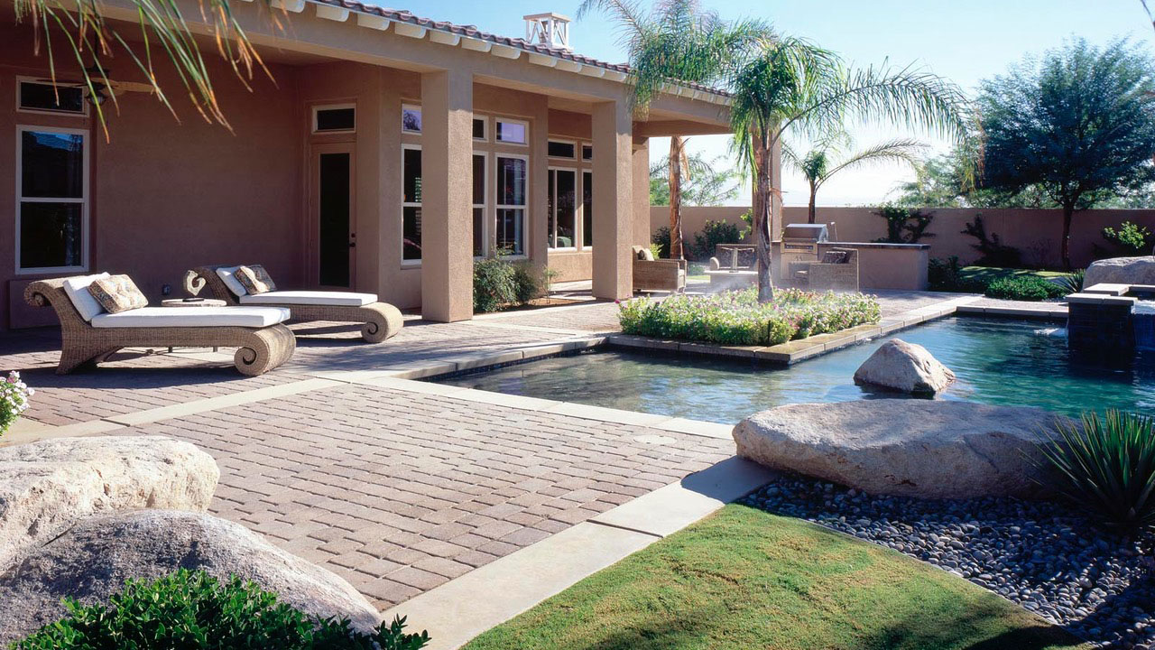 Gorgeous pool deck pavers in outdoor living space with lawn chairs and turf