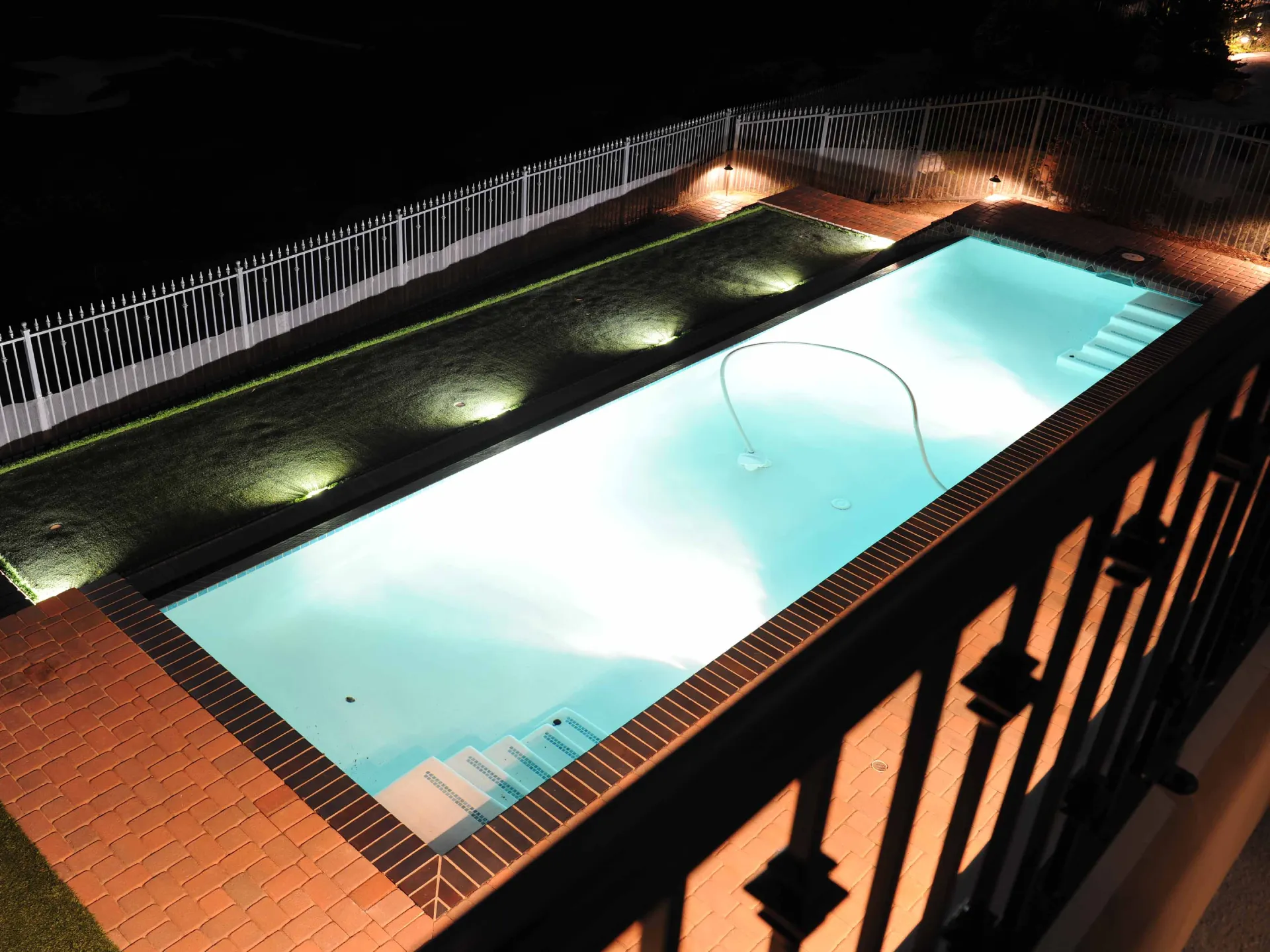 Pool with outdoor lights illuminating patio and walkway.