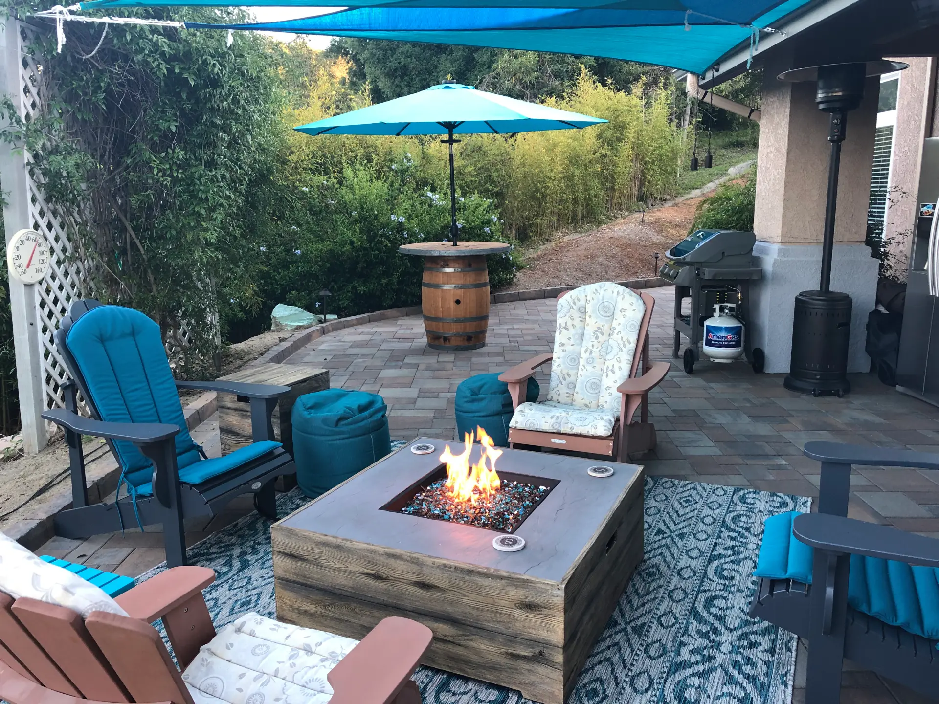 Stone wall fire pit surrounded by chairs and an umbrella on top of a paved patio.