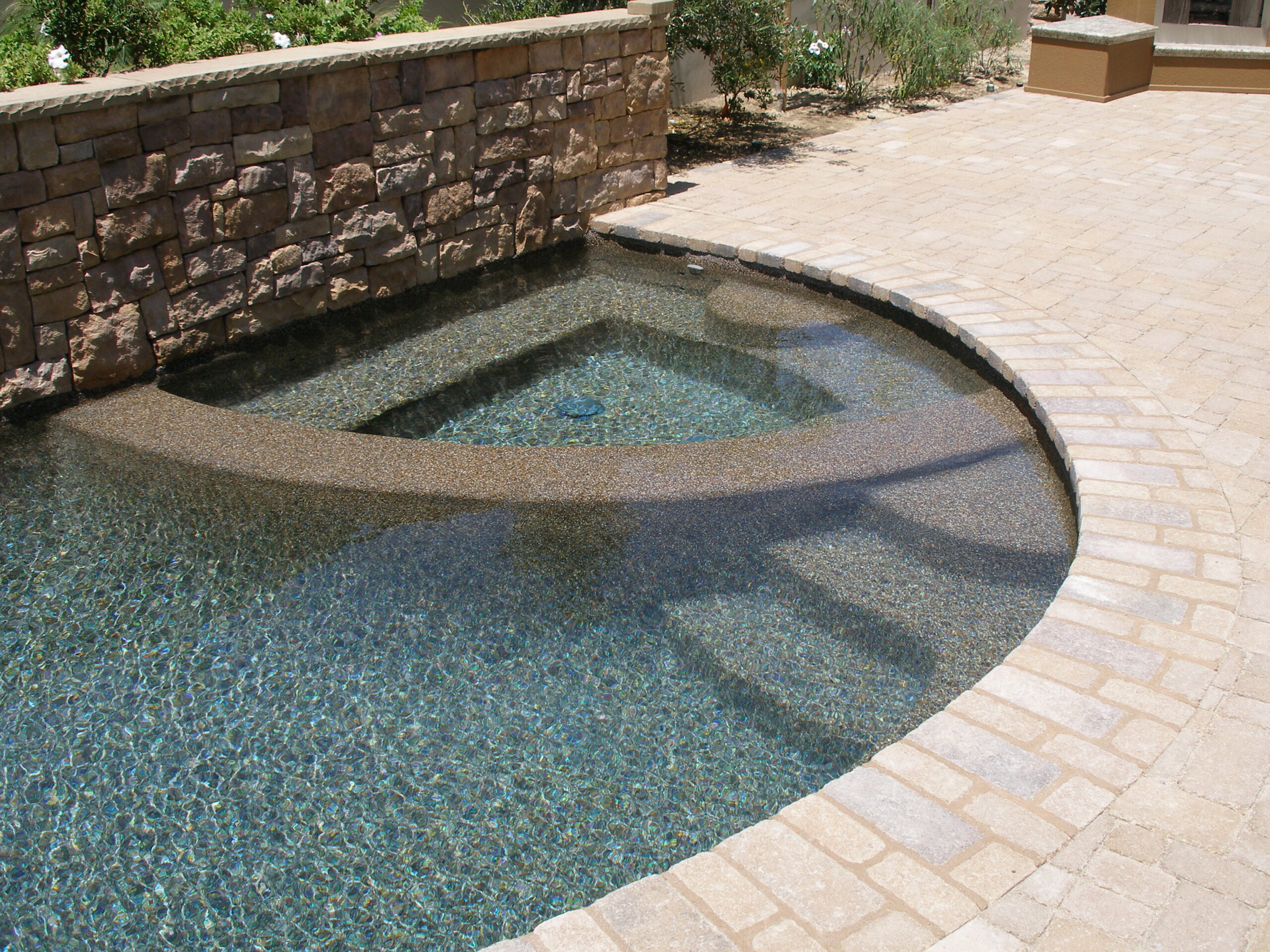 Gorgeous Pool with stone steps next to concrete pavers and stone wall.